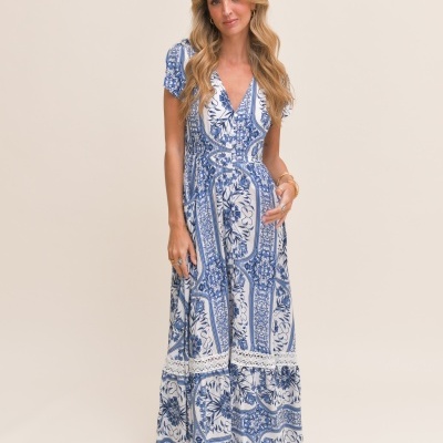 Vestido comprido azul e branco com padrão estampado e decote em V, usado por mulher em fundo creme.