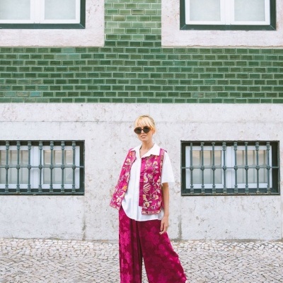 Mulher com roupa rosa e branca em calçada portuguesa à frente de parede verde com azulejos.