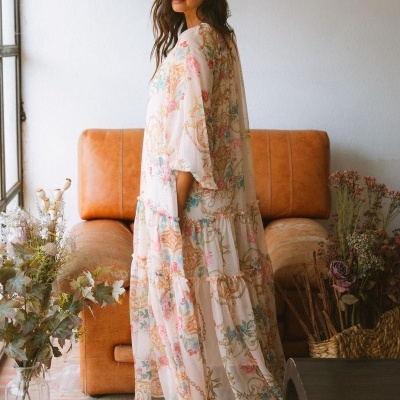 Vestido comprido floral com padrão em tons pastel num interior com sofá castanho e flores secas