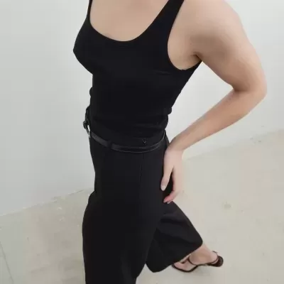 Pessoa com top preto de alças, calças pretas largas, cinto preto e sandálias pretas em chão claro