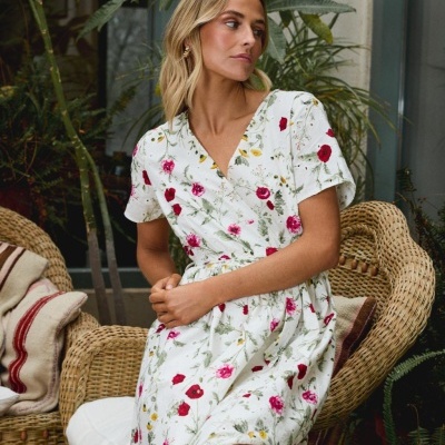 Vestido branco com flores coloridas usado por mulher sentada em cadeira de vime