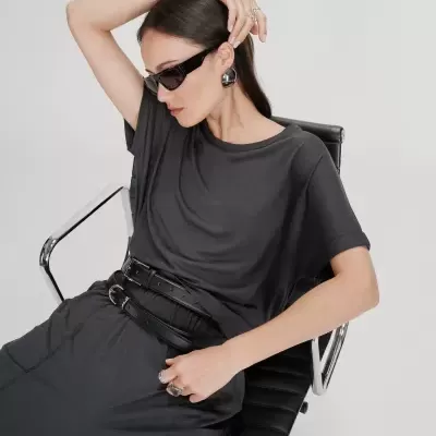 Mulher com roupa preta, óculos de sol e acessórios metálicos sentada numa cadeira de escritório.