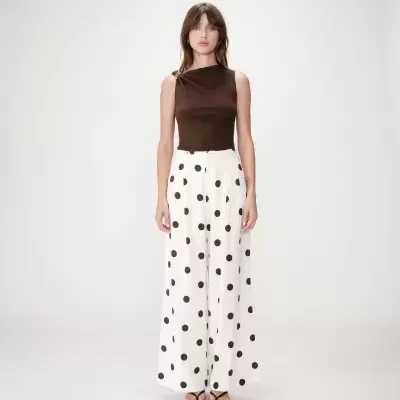Modelo veste top castanho sem mangas e calças largas brancas com bolinhas castanhas.