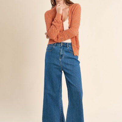 Mulher com camisola de malha terracota, calças de ganga largas azuis e sandálias castanhas