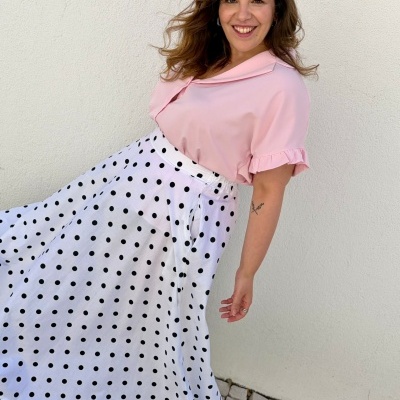 Vestido rosa claro com saia branca de bolinhas pretas usado por mulher sorridente próximo a parede branca