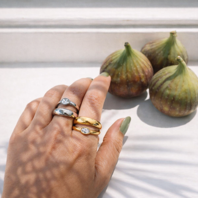 Mão com anéis dourados e prateados e figos ao lado