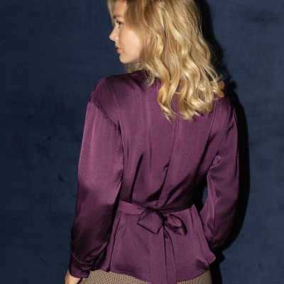 Blusa roxa acetinada com cinto nas costas e calções curtos pied-de-poule em fundo azul.