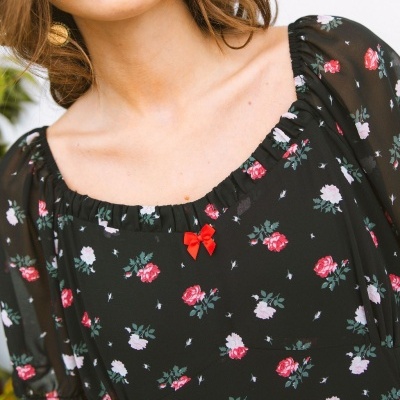 Vestido preto com flores rosas e verdes e laço vermelho no centro do decote.