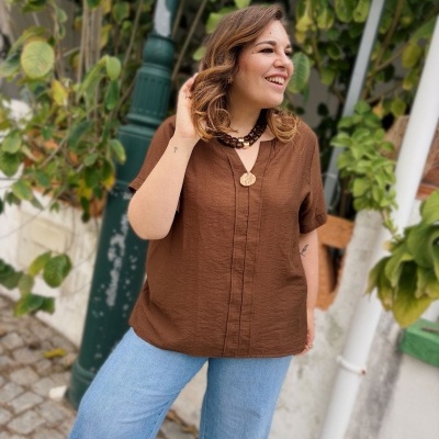 Blusa castanha texturizada com botões e decote em V num ambiente exterior