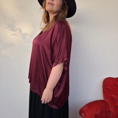 Pessoa com blusa bordô, saia preta e chapéu preto junto a poltrona vermelha