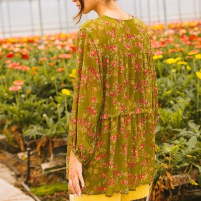 Blusa verde floral transparente com mangas compridas vista de costas numa estufa com flores