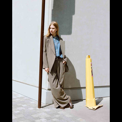 Mulher com fato xadrez castanho claro ao lado de cone amarelo com texto