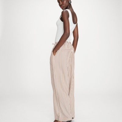 Mulher de lado a usar top branco canelado e calças largas às riscas brancas e castanhas