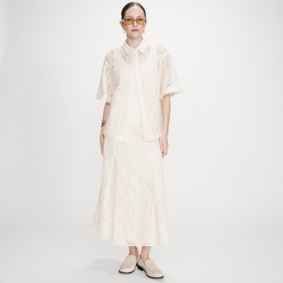 Modelo a usar camisa e saia branca de renda com sapatos bege e óculos com lentes amarelas
