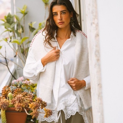 Mulher com camisa branca e colete de malha numa varanda com plantas suculentas