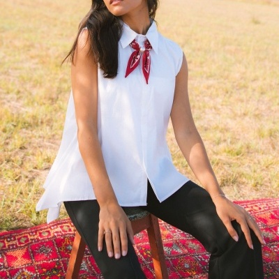mulher com blusa branca sem mangas e laço vermelho sentada em banco sobre tapete vermelho num campo aberto
