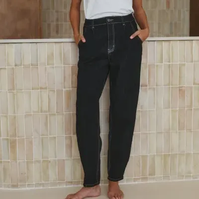 Pessoa com t-shirt branca e calças de ganga pretas em fundo de azulejos neutros