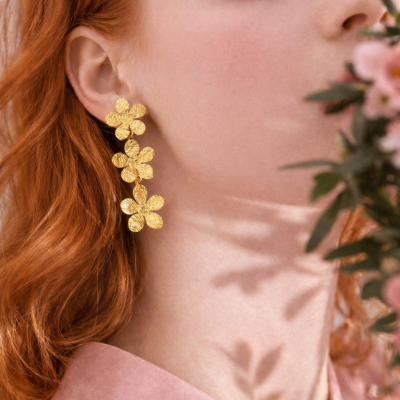 Brincos dourados em forma de flores usados por mulher com cabelo ruivo