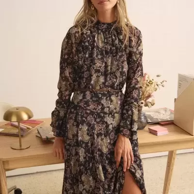 Vestido comprido florido com cinto fino em ambiente interior junto a secretária de madeira