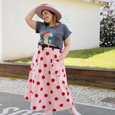 Mulher com chapéu rosa, camiseta cinza, saia rosa com bolinhas vermelhas e ténis rosa