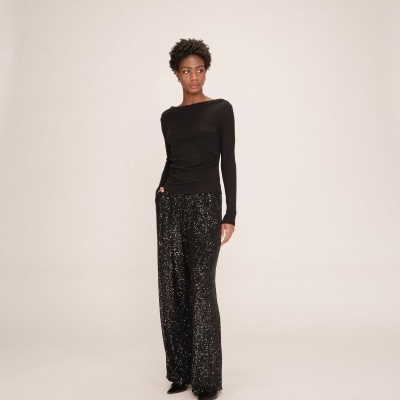 Mulher com camisa preta manga comprida e calças pretas com lantejoulas brilhantes