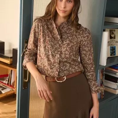 Mulher a usar blusa floral castanha e saia castanha com cinto em ambiente interior