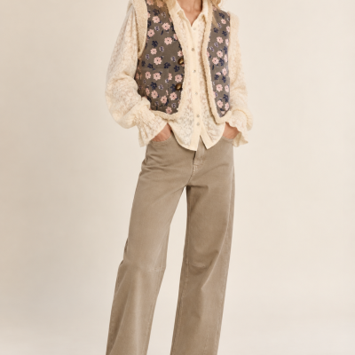 Mulher com colete floral, camisa rendada, calças largas bege e botins castanhos