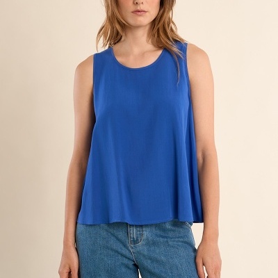 Camisola azul sem mangas com decote redondo, jeans azuis, fundo bege