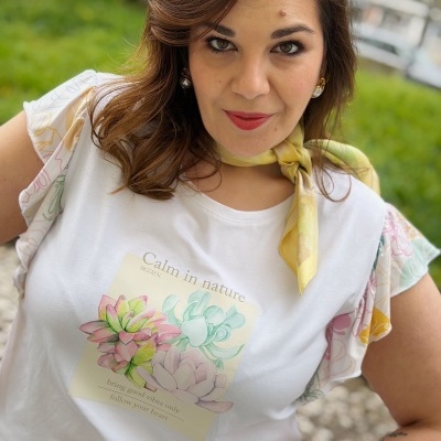T-shirt branca com estampa de flores e texto, mangas com padrão floral e lenço amarelo ao pescoço