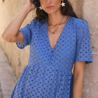 Vestido azul com padrão de buracos usados por mulher ao lado de parede de pedra