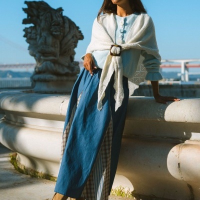 Mulher com roupa de malha e saia junto a fonte de pedra ao ar livre