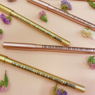 Canetas delineadoras douradas e rosa metalizado com texto preto e flores secas coloridas.