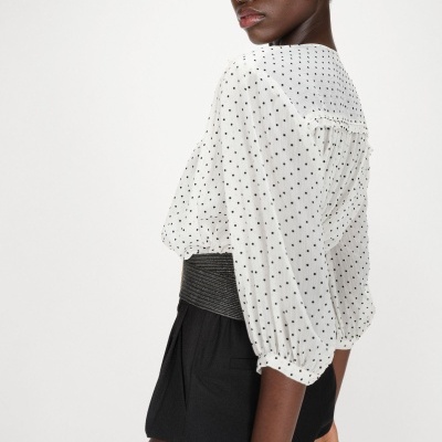 Mulher com blusa branca de pontos pretos e calções pretos