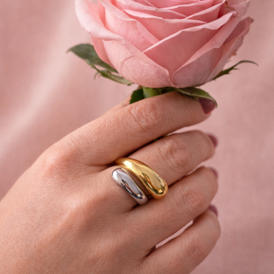 Anel duplo liso prateado e dourado na mão segurando uma rosa cor-de-rosa.