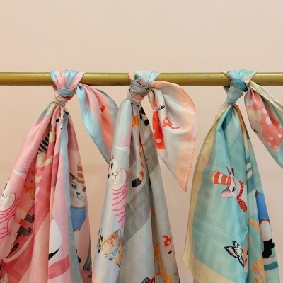 Lenços decorativos com padrões de gatos coloridos pendurados num suporte dourado