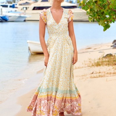 Vestido comprido florido com decote em V e mangas curtas, em ambiente de praia com barcos e vegetação
