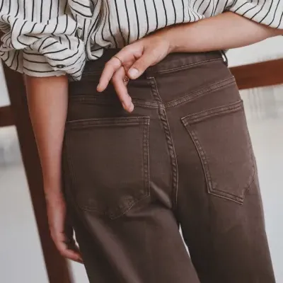 Calças castanhas com bolsos traseiros e camisa branca de riscas pretas