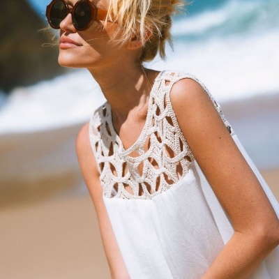 Vestido branco com crochê bege na parte superior e óculos de sol castanhos, mulher na praia