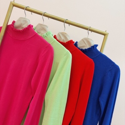 Quatro camisolas de gola alta coloridas penduradas num cabide de madeira.