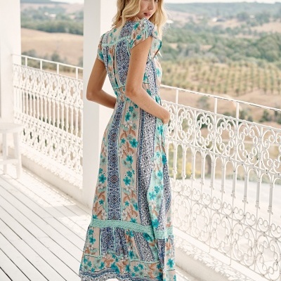 Mulher de vestido floral longo em varanda branca com vista para campo