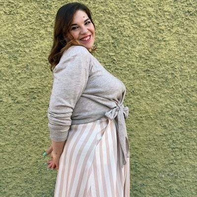 Mulher com blusa cinzenta e saia às riscas brancas e bege num fundo verde.