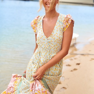 Vestido fluido com padrão floral em tons pastel numa praia