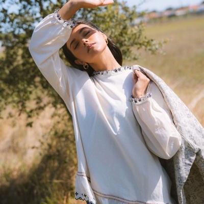 Mulher a usar blusa branca bordada com mangas compridas ao ar livre, com fundo de campo e árvore