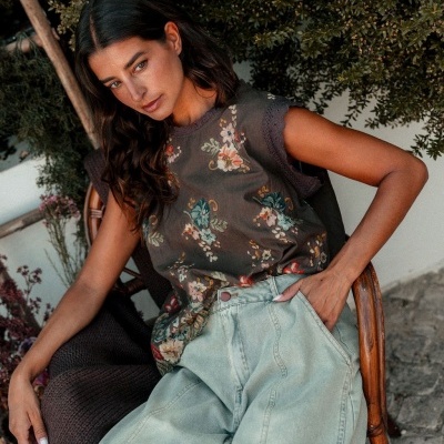Mulher sentada com blusa floral e calças de ganga cinza claro
