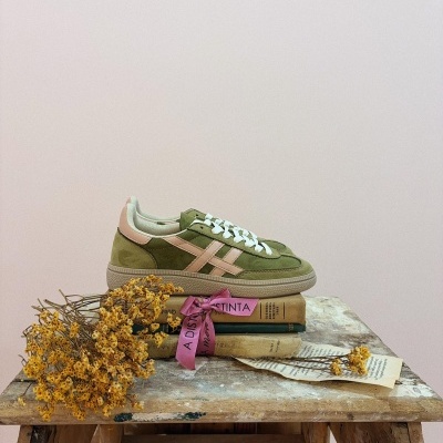 Ténis verdes com detalhes rosa e atacadores brancos sobre uma mesa de madeira rústica com flores e livros