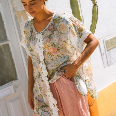 Mulher a usar blusa floral com renda branca e calças largas cor de rosa num ambiente exterior urbano.