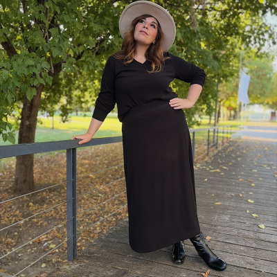 Mulher com roupa preta e chapéu bege em varanda de madeira junto a árvores