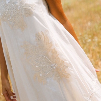 Vestido branco com bordados florais e detalhes em lantejoulas em ambiente de campo
