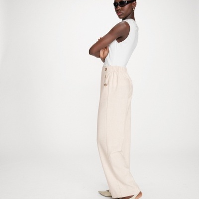 Mulher com calças largas bege, top branco e óculos escuros