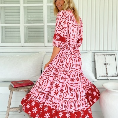 Vestido longo vermelho e rosa com padrão floral e linhas onduladas, modelo num ambiente interior branco.